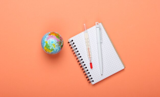 Het probleem van de opwarming van de aarde. Globe, thermometer met een notitieboekje op oranje achtergrond. Bovenaanzicht