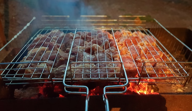 Het proces van het koken van shish kebab op de grill. Sappig en geurig vlees kwijnt weg bij vuur en rook. Platteland picknick concept 's nachts. Smakelijk en voedzaam picknickgerecht in de open lucht.