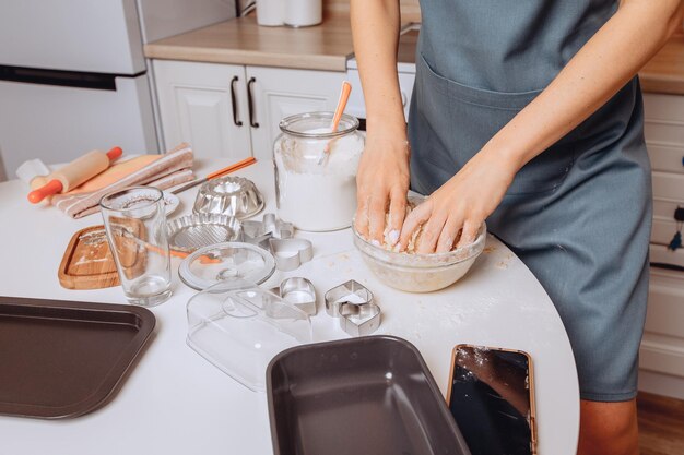 Het proces van het maken van deeg voor een maaltijd close-up. Een jonge huisvrouw in een schort kneedt deeg in een kom met haar handen. Zelf de ingrediënten mixen. Het concept van koken en bakken.