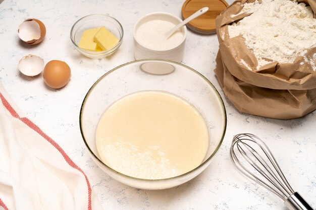 Het proces van het maken van deeg voor pannenkoeken met ingrediënten op een lichte tafel, eieren en bloem worden opgeklopt met een mixer.