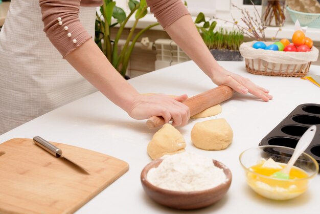 Het proces van het uitrollen van het deeg thuis op tafel is de handen van een vrouw voor het maken van cruffins feestelijke gebakjes voor Pasen. zijaanzicht van een lichte keuken, met beschilderde eieren.