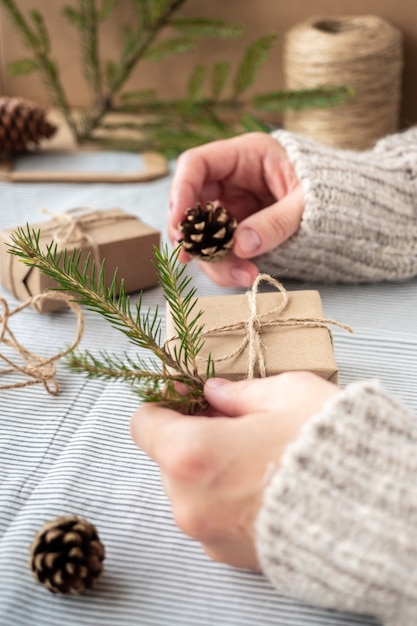 Het proces van het verpakken van stijlvolle, moderne cadeaus voor Kerstmis en Nieuwjaar. Geschenkdoosjes van kraftpapier, touw en kerstboomtakken. Kerst achtergrond, vakantie sfeer.