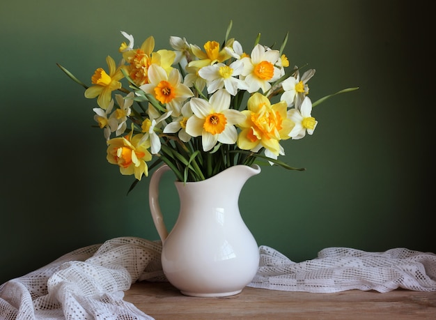 Het rassenboeket van gele gele narcissen in een witte kruik op een groene achtergrond.