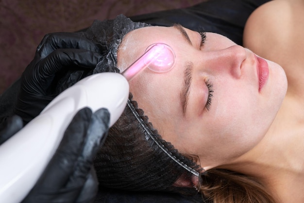 het reinigen van de huid op het voorhoofd van een patiënt in de spa met behulp van hoogfrequente pulsstromen