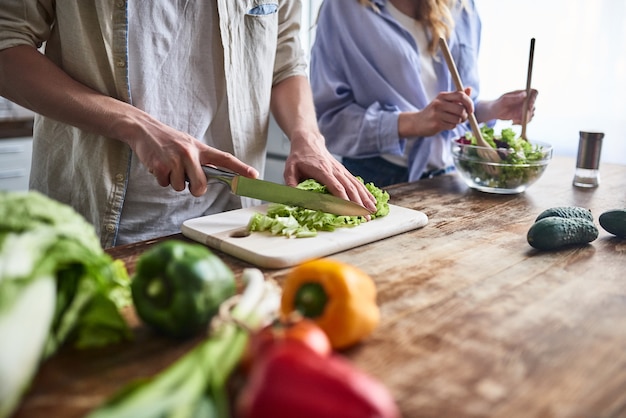 Het romantische paar kookt op keuken. knappe man en aantrekkelijke jonge vrouw hebben samen plezier tijdens het maken van salade. gezond levensstijlconcept.