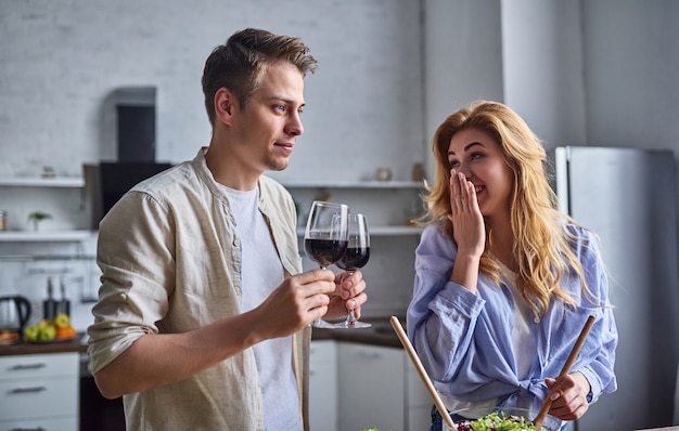 Het romantische paar kookt op keuken. Knappe man en aantrekkelijke jonge vrouw hebben samen plezier tijdens het maken van salade. Gezond levensstijlconcept.