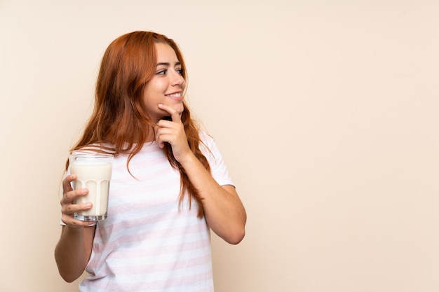 Het roodharigemeisje dat van de tiener een glas melk over geïsoleerde een idee denkt en kant kijkt als achtergrond