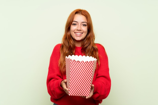 Het roodharigemeisje van de tiener met sweater die een kom popcorns houdt