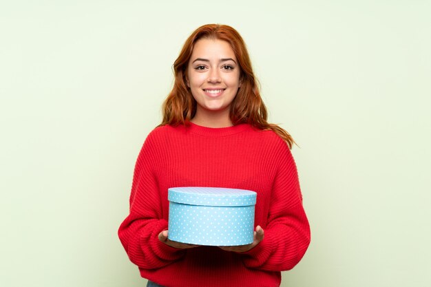 Het roodharigemeisje van de tiener met sweater over de geïsoleerde groene doos van de achtergrondholdingsgift