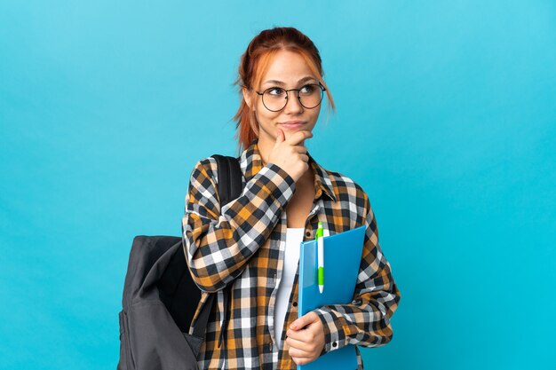 Het Russische meisje van de tienerstudent dat op blauwe muur wordt geïsoleerd die een idee denkt terwijl het omhoog kijken