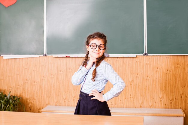 Het schoolmeisje met een bril staat bij het bord en lacht