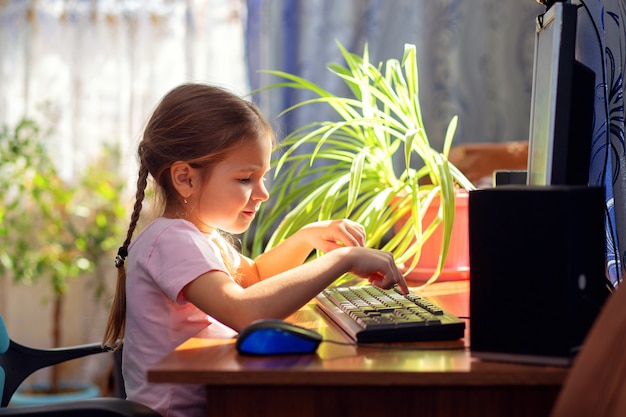 Het schoolmeisje van het meisje zit thuis bij een computerbureau en houdt zich bezig met een bureaucomputer.