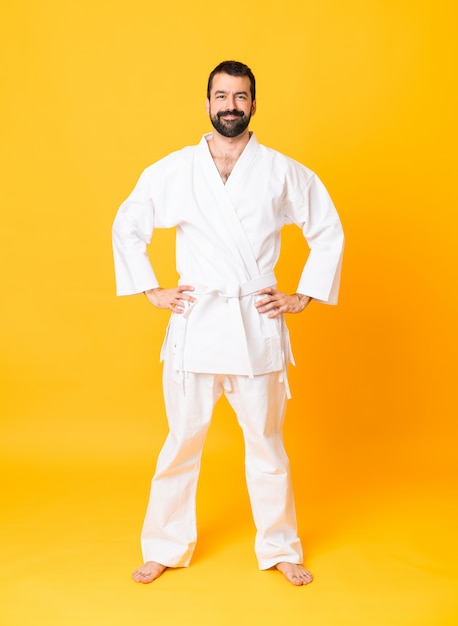 Het schot van gemiddelde lengte van de mens over geïsoleerde gele achtergrond die karate het stellen met wapens doen bij heup en het glimlachen