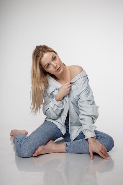 Het sexy kaukasische meisje stellen in jeans en overhemd op witte studio