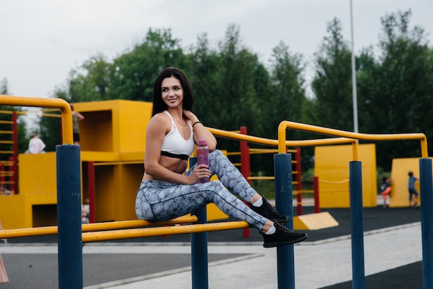 Het sexy meisje doet sporten en drinkt water in openlucht. Fitness. Gezonde levensstijl