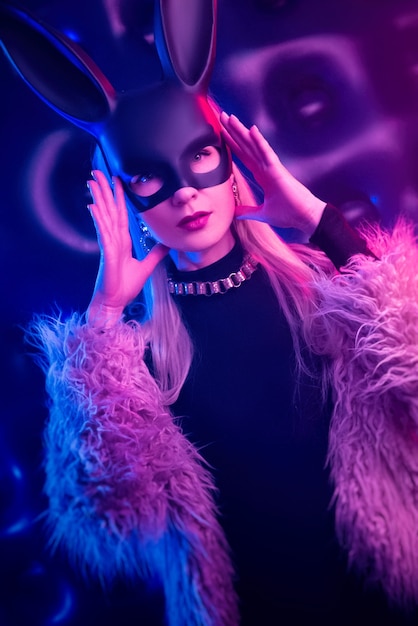 Het sexy meisje in een bodysuit en bontjas met een konijnenmasker in het neonlicht