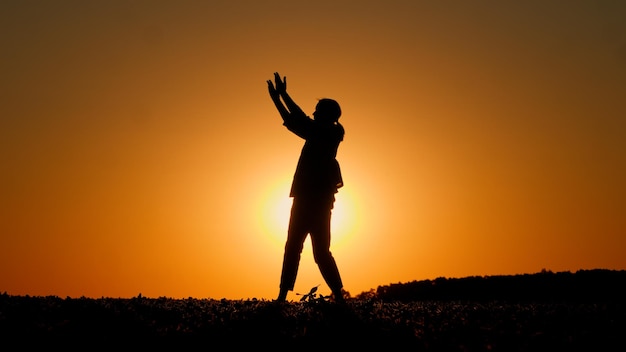 Foto het silhouet van een jonge vurige vrouw danst in een veld bij zonsondergang gemarkeerd door de oranje hemel