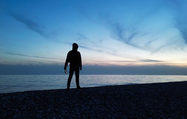 Het silhouet van een man bij een prachtige zonsondergang tegen de achtergrond van de zee en de wolken in zijn hand is een afstandsbediening van een drone