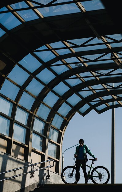 Het silhouet van een vrouw met een fiets op de trappen tegen de blauwe lucht.