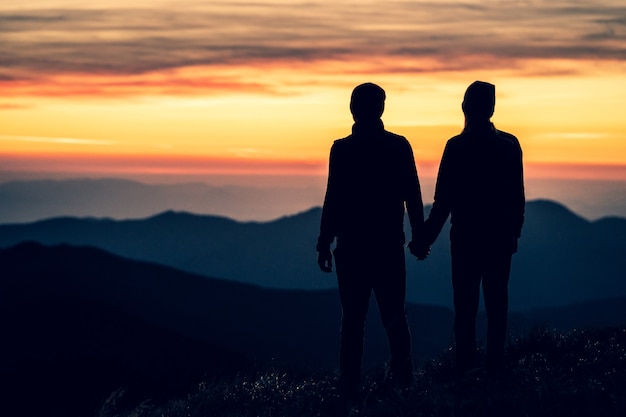 Het silhouet van het paar op de berg met een zonsondergangachtergrond