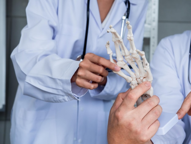 Het skeletmodel van de menselijke hand of pols op het bureau, wijzend door een volwassen mannelijke arts, geeft kennis aan de vrouwelijke arts Twee artsen in witte uniformen praten samen in een medisch kantoor