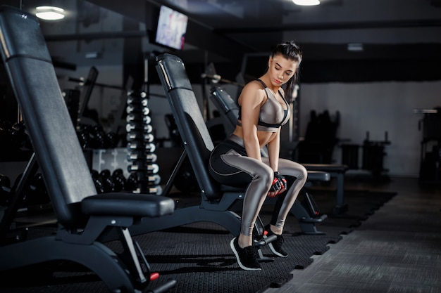 Het slanke, bodybuildermeisje, heft zware domoor op die zich voor de spiegel bevindt terwijl in de gymnastiek opleidt. Sportconcept, vetverbranding en een gezonde levensstijl