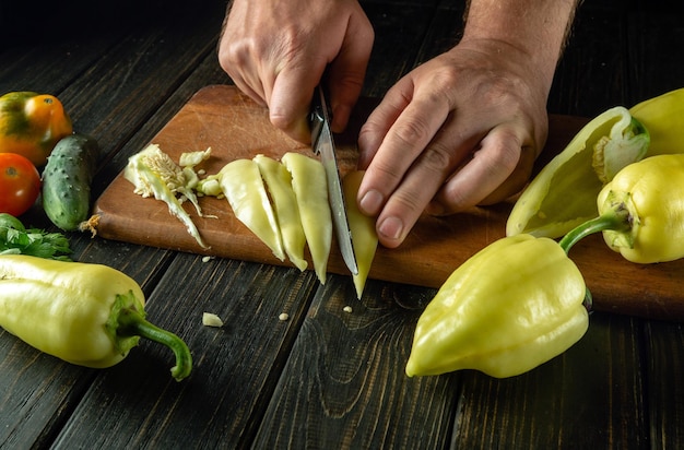 Het snijden van een rijpe peper door de handen van de chef-kok voordat het op de keukentafel wordt gesneden Concept van het koken van groente lecho of vegetarisch gerecht