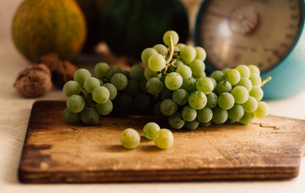 Het stilleven van de herfst De groene druiven liggen op houten raad Op de achtergrond zijn pompoenen, okkernoten en schalen Het concept van de de herfstoogst Gelukkige Thanksgiving Selectieve nadruk Horizontale oriëntatie.