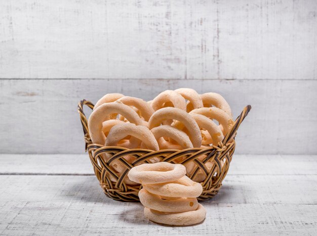 Het strooikoekje gemaakt met cassavezetmeel in een mand boven wit hout met wat gevallen koekjes ervoor (biscoito polvilho).