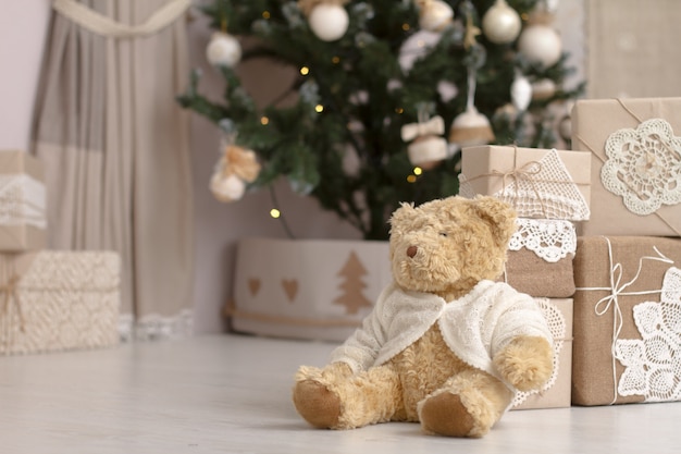 Het stuk speelgoed van de close-up Teddybeer dichtbij de berg van giften die in ambachtdocument worden ingepakt op een vage achtergrond van een verfraaide Kerstboom.