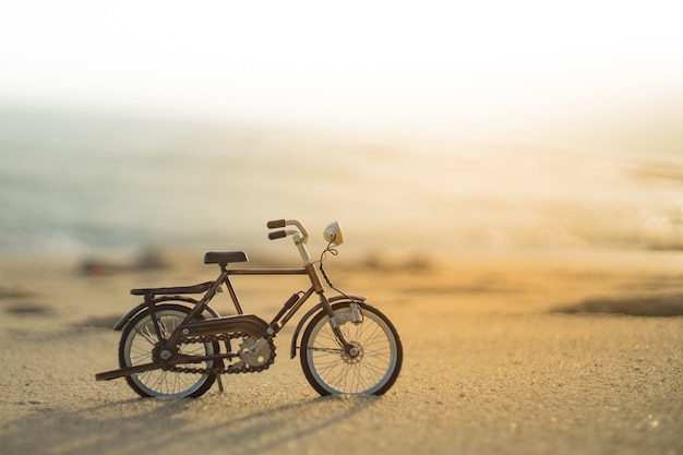 Het stuk speelgoed van het fietstransport op zand overzees strand in de avond zonsonderganghemel