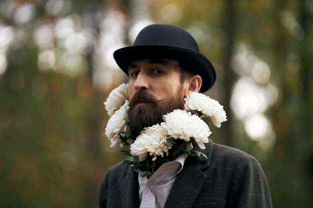 Het surrealistische thema een bebaarde man in een blazer en hoed met een boeket witte bloemen om zijn nek