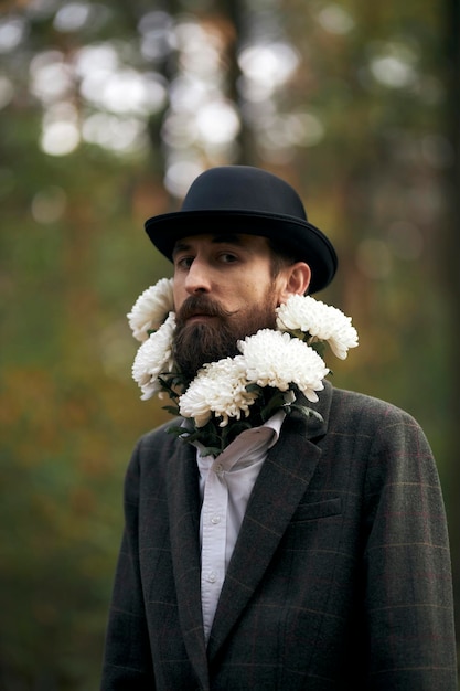 Het surrealistische thema een bebaarde man in een blazer en hoed met een boeket witte bloemen om zijn nek