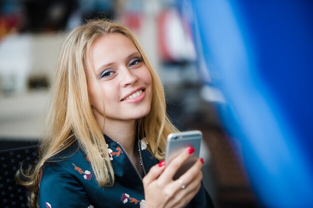 Het texting van het meisje op de slimme telefoon in een restaurantterras met een ongericht achtergrond