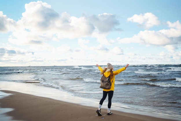 Het toeriste meisje in een geel jasje poseert bij de zee Reizigend levensstijl avontuur