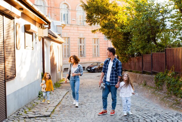Het toeristengezin van vier personen gaat de straat op van de oude stad De man, de vrouw en twee kleine meisjes lopen door een Europese stad