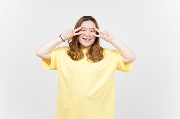 Het tonen van vredesteken van mooie Aziatische vrouw, gekleed in gele TShirt geïsoleerd op een witte achtergrond