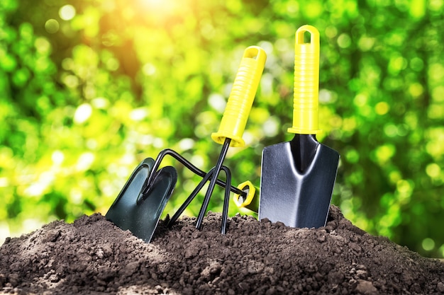 Het tuingereedschap harkt schop en bijl op stapel van aarde onder heldere zon