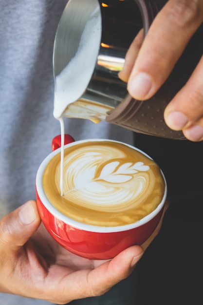 Het verticale beeld van het gieten van melk aan espresso maakt latte kunst op rode kopkoffie