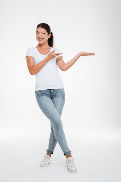 Het volledige lengte glimlachende model in t-shirt en jeans isoleerde witte muur