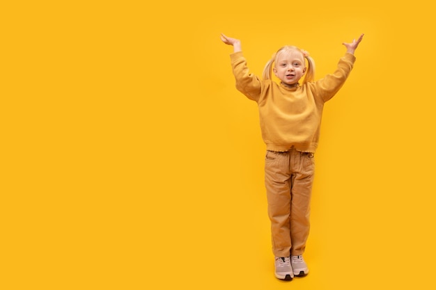 Het volledige portret van een voorschools meisje in gele kleren hief haar handen op en leek iets vast te houden