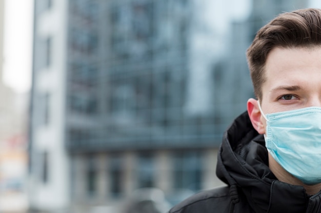 Foto het vooraanzicht van de mens die medisch masker met defocused stad draagt