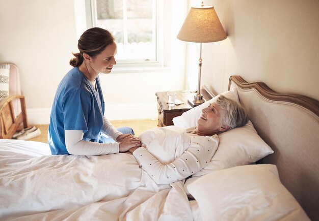 Het vriendelijkste gezicht om wakker van te worden Shot van een jonge verpleegster die in bed praat met een oudere vrouw in een bejaardentehuis