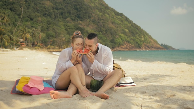 Het vrolijke liefdespaar dat plakjes watermeloen vasthoudt en eet op de zee van het tropische zandstrand