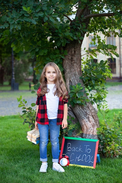 Het vrolijke schoolmeisje houdt stapel boeken in tuin dichtbij school.