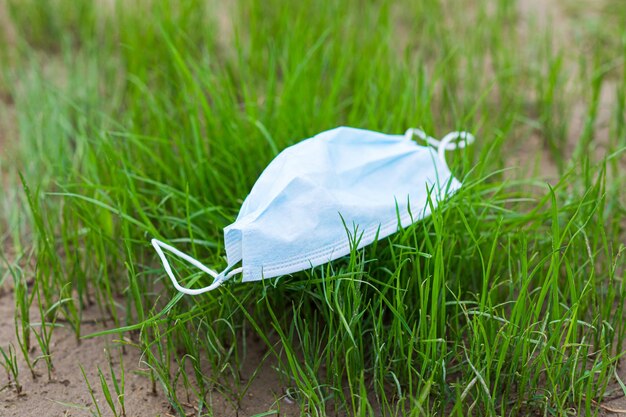 Het weggegooide beschermende masker ligt op het groene gras Het concept van een tweede uitbraak van de epidemie