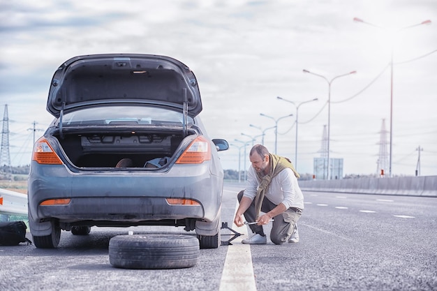 Het wiel van een auto op de weg vervangen. Een man doet bandenwerk aan de zijlijn.