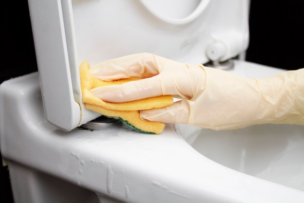 Het wijfje dient een handschoen met een spons voor het wassen van close-up in. Een vrouw wast een wit toilet met een gele spons.