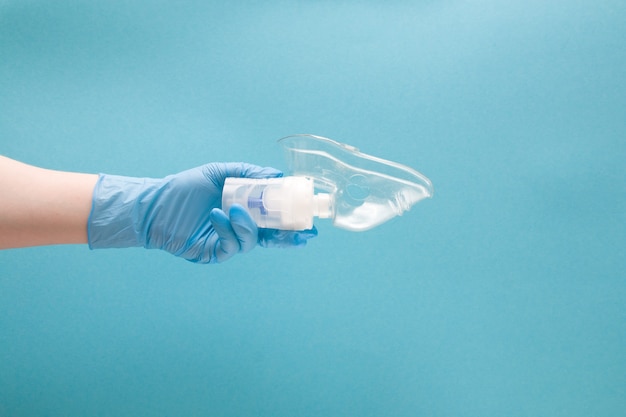 Het wijfje dient handschoen in houdt het reservoir van de verstuiversdrug met siliconemasker, blauwe achtergrond, exemplaarruimte