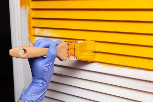 Het wijfje dient rubberhandschoen met borstel in schilderend houten deur met gele verf